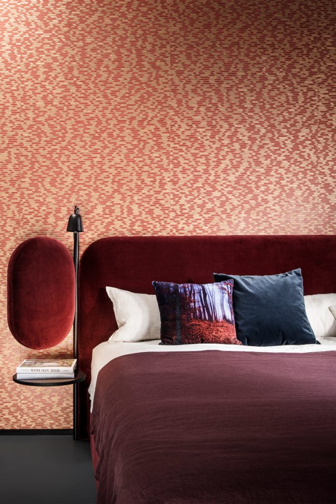 a red and yellow print behind a red velvet double bed with a maroon duvet cover