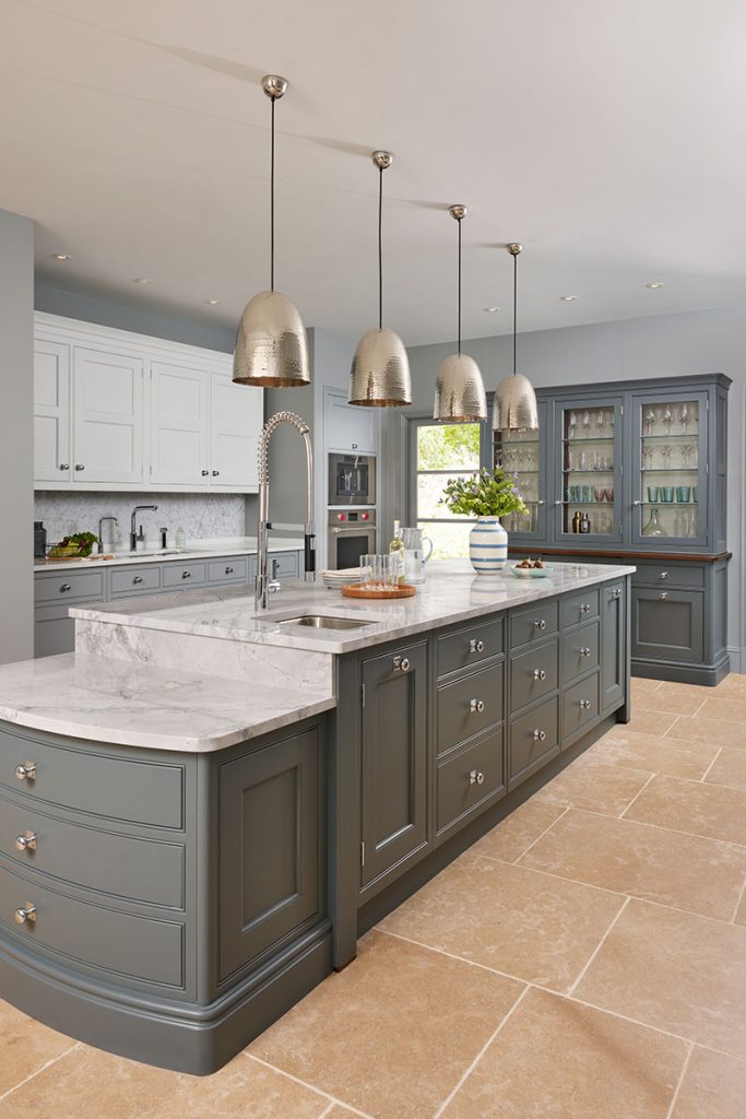 a white marble island with traditional grey cabinetry with silver knobs under four gold pendant lights to illustrate a feature on kitchen must-haves for entertaining