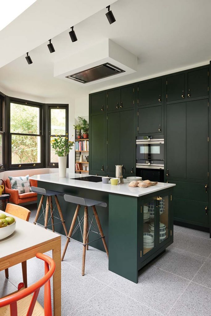 forest green kitchen units and black appliances in front of a white island with grey wooden bar stools, illustrating how to make your kitchen bigger