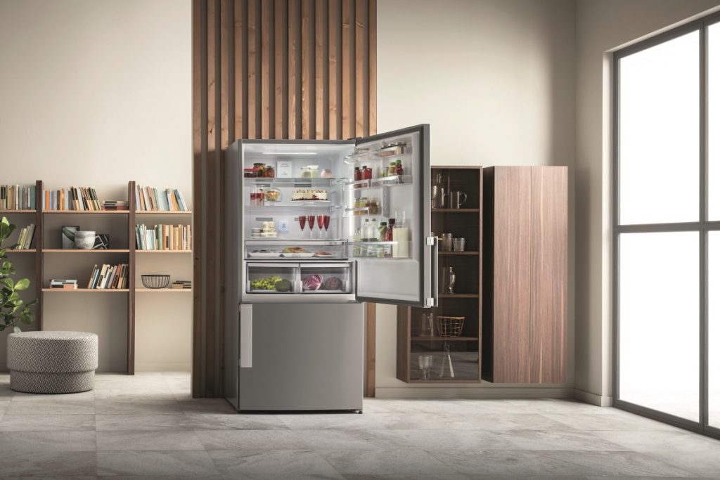 a freestanding silver fridge in front of a wooden panel in a kitchen featuring lots of wooden shelves and books