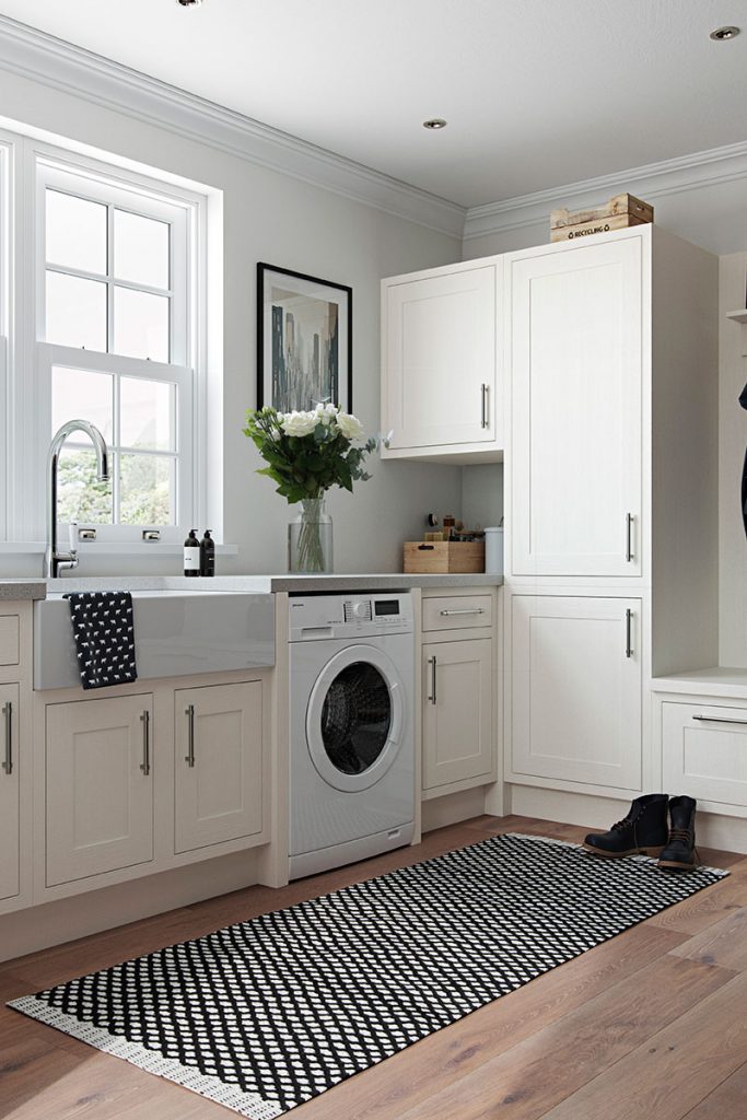 a kitchen featuring cream Shaker cabinetry with silver pull handles, a silver tap in a white Belfast sink, a washing machine, and a bunch of white roses on the grey worktop, to illustrate a feature on kitchen must-haves for entertaining