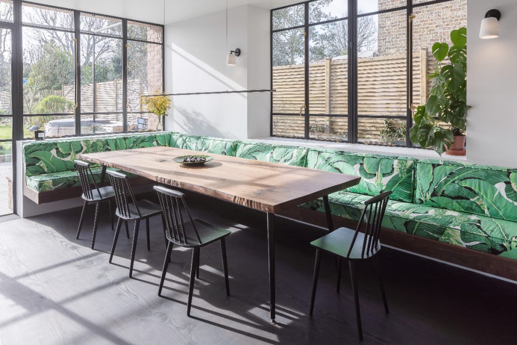 banquette seating in front of black glazing with a tropical green print behind a walnut table with black traditional chairs around it