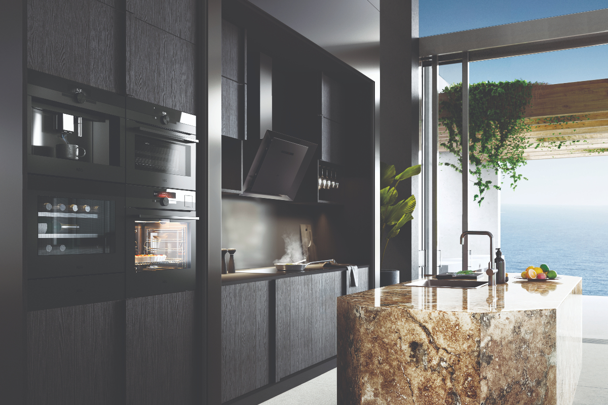 black handleless cabinetry featuring built-in appliances next to a stone island in a kitchen with a sea view