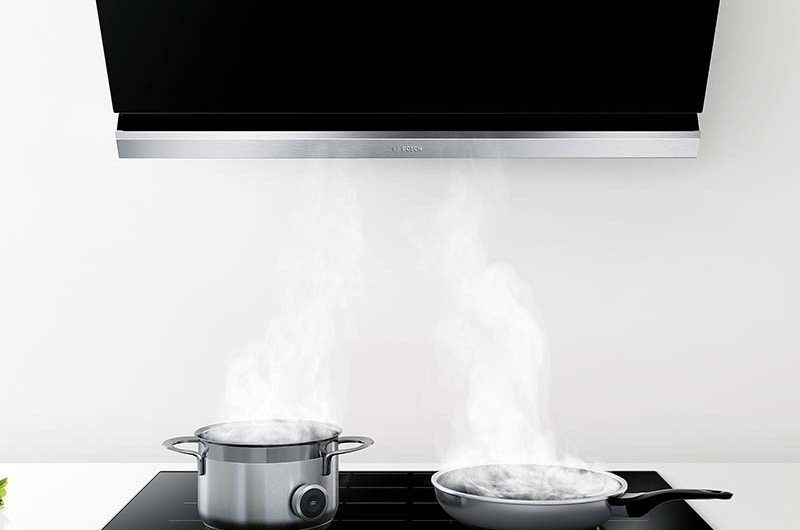 a black Bosch extractor above a black induction hob with steaming stainless steel pans on it