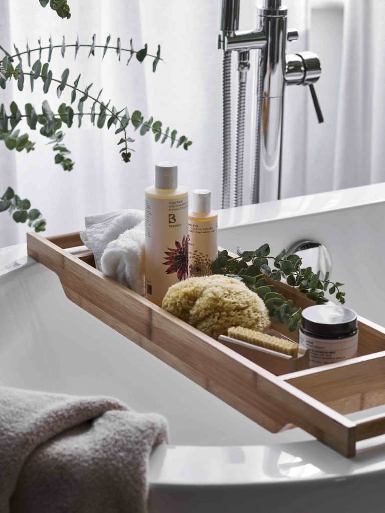 a bath board full of toiletries and accessories across a white bath 
