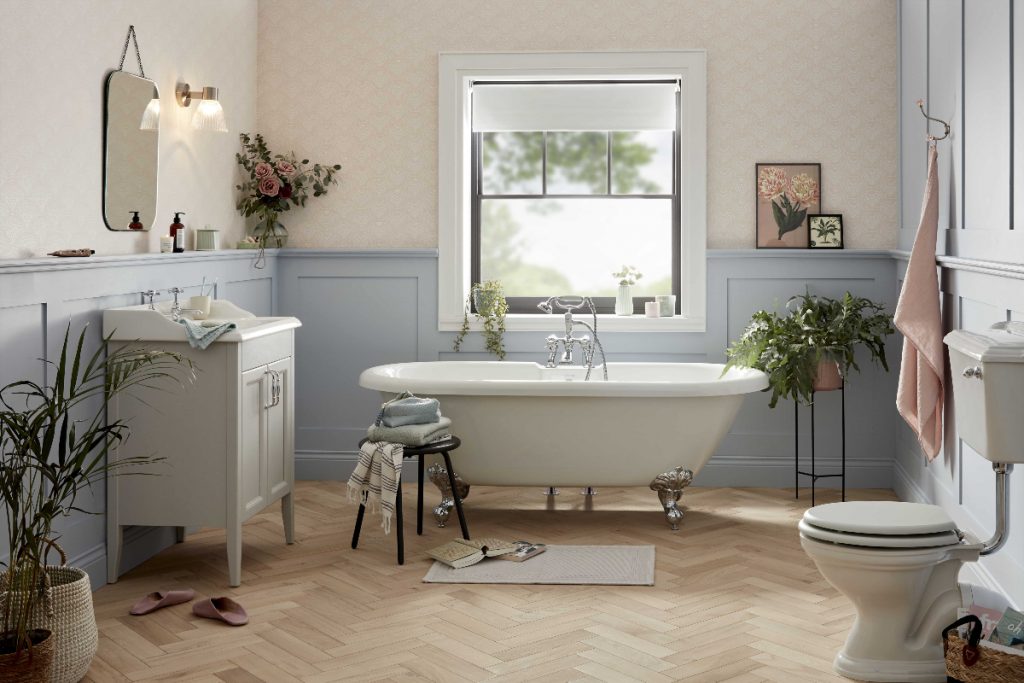 an acrylic double ended roll top bath with silver claw feet in a big room with herringbone flooring, a loo and a vanity unit with basin