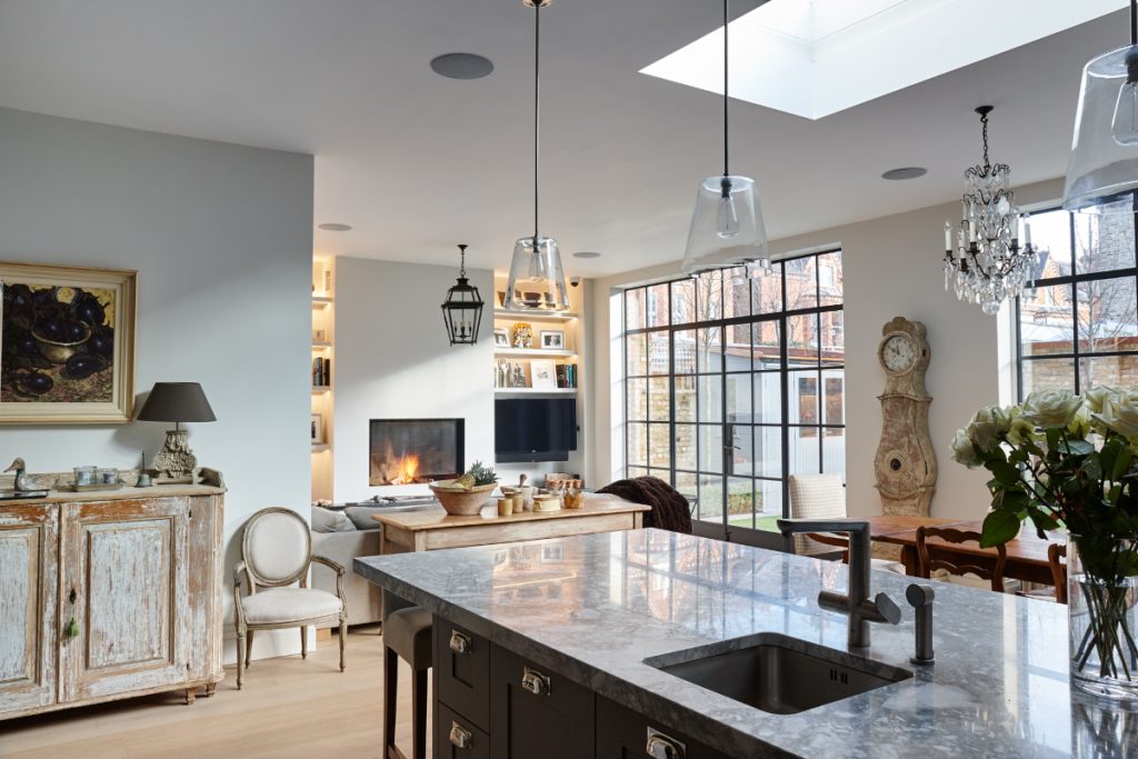 a very large kitchen featuring steel-framed glazing and pendant lights over a marble island, illustrating how to make your kitchen bigger