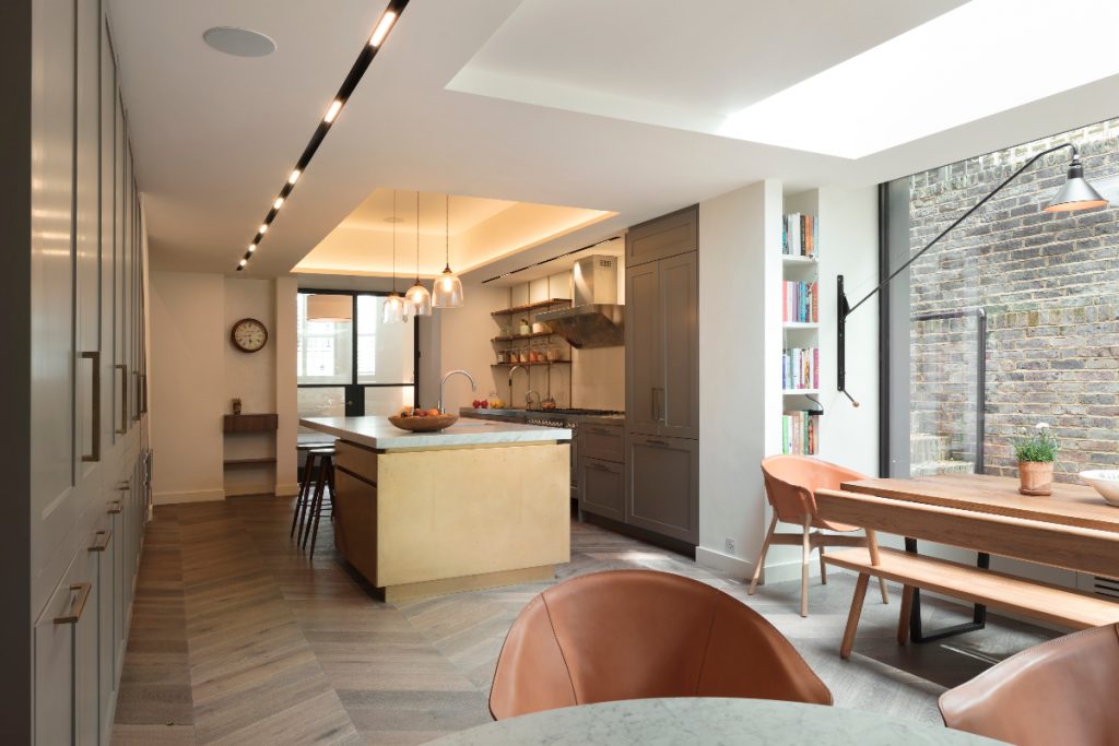 a wooden island with a marble worktop and three pendant lights above it, grey cabinetry and an extractor fan in a large extension with herringbone flooring