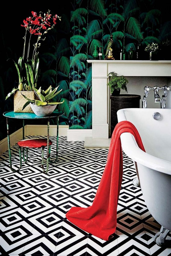 a black room with a green tropical print on the walls, monochrome geometric flooring, a freestanding roll top tub and several plants and accessories