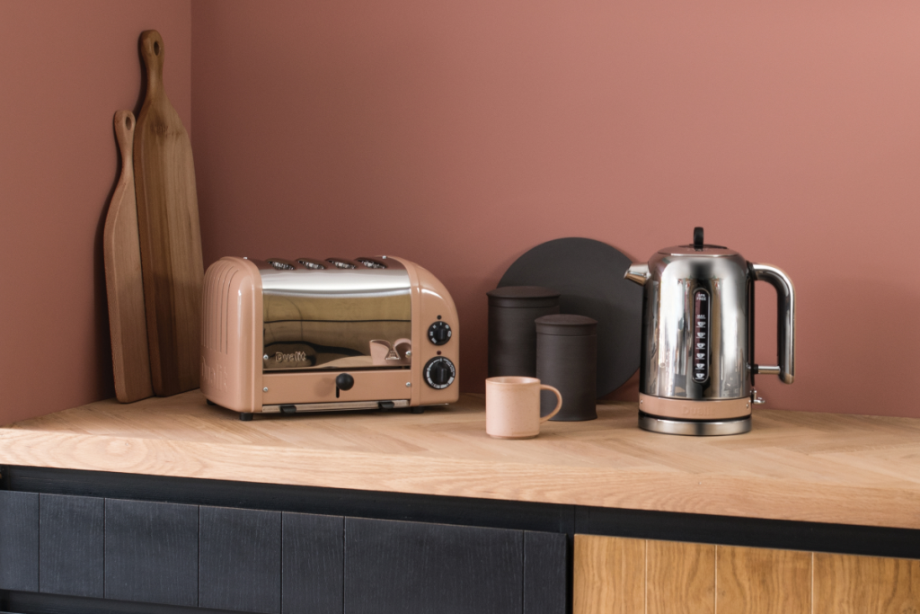 metallic toaster and kettle set on a wooden worktop next to chopping boards and a pink wall