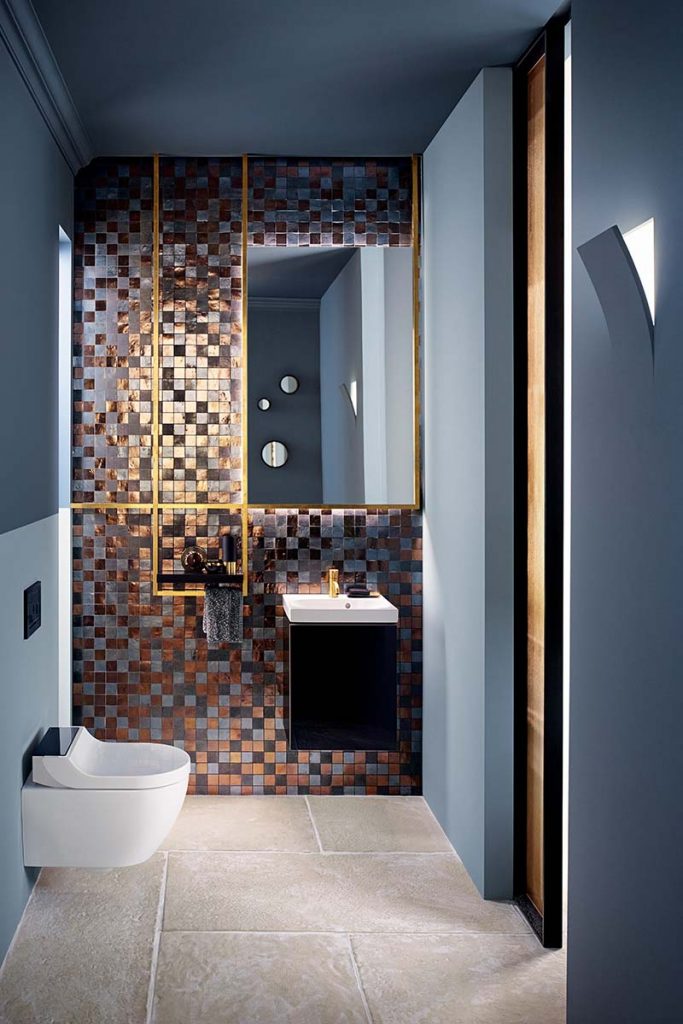 a maximalist bathroom featuring bronze-toned mosaic tiles and black and white sanitaryware