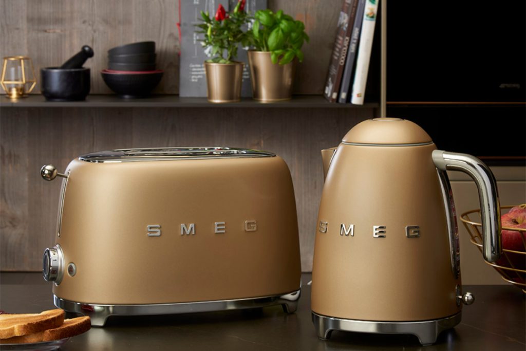 SMEG matte champagne gold appliances on a worktop under a shelf full of books and plants