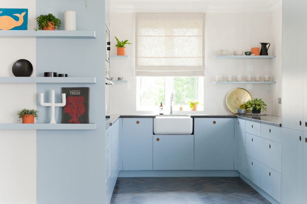 a small kitchen with powder blue cabinetry, open shelving and a white window blind