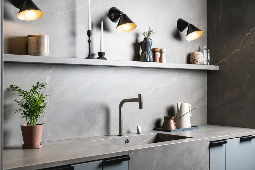 a small kitchen featuring a grey marble splashback and cabinetry and open shelving for candles and utensils