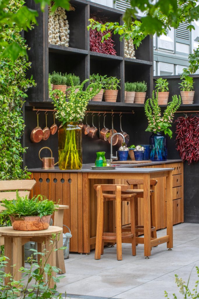 A Dekton Trillium worktop featuring an inbuilt sink with silver tap, copper pans hung in a row above it and numerous green plants in pots dotted above and around it