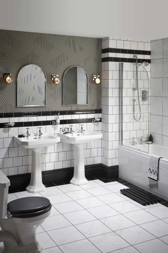 an Art Deco bathroom featuring white metro tiles, gold geometrical tiles and two white pedestal basins