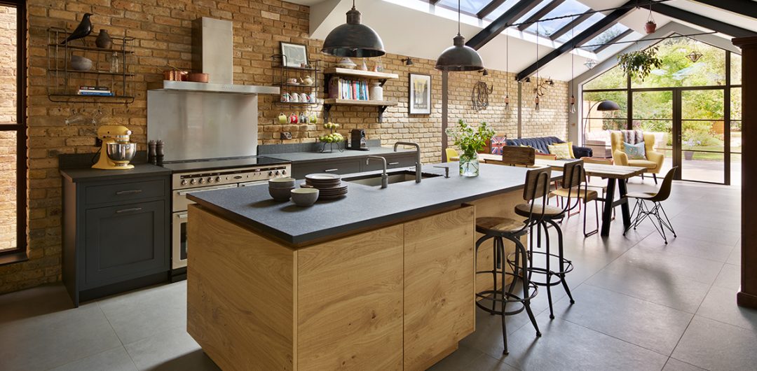 a modern rustic kitchen featuring a dark grey island with wooden cabinetry and three charcoal pendant lights above it, illustrating how to make your kitchen bigger