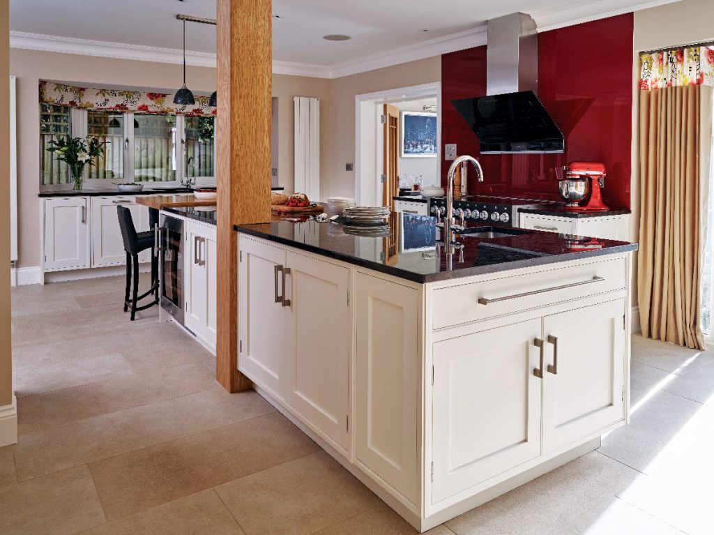 an open plan design featuring cream cabinetry with traditional brass handles, a red splashback, a red kitchen mixer and black appliances above a wooden floor