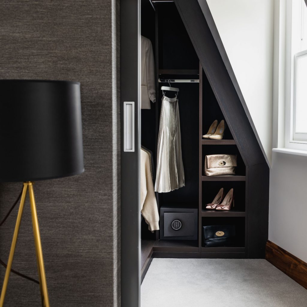 a dark walnut wood bespoke brown wardrobe with shoes, bags and a silk skirt hanging up in it