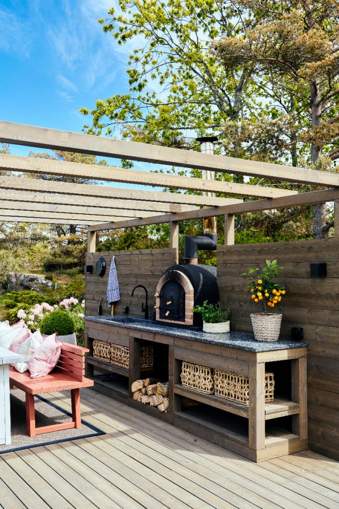 a royal natural stone worktop featuring storage underneath and plants above within a wooden framework, behind a red bench with pink and grey cushions