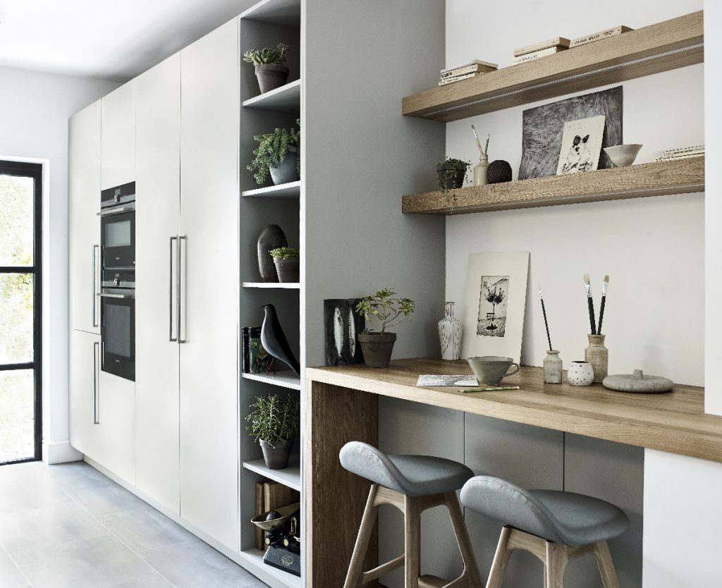 an oak breakfast bar with grey stools next to white cabinetry with open shelving