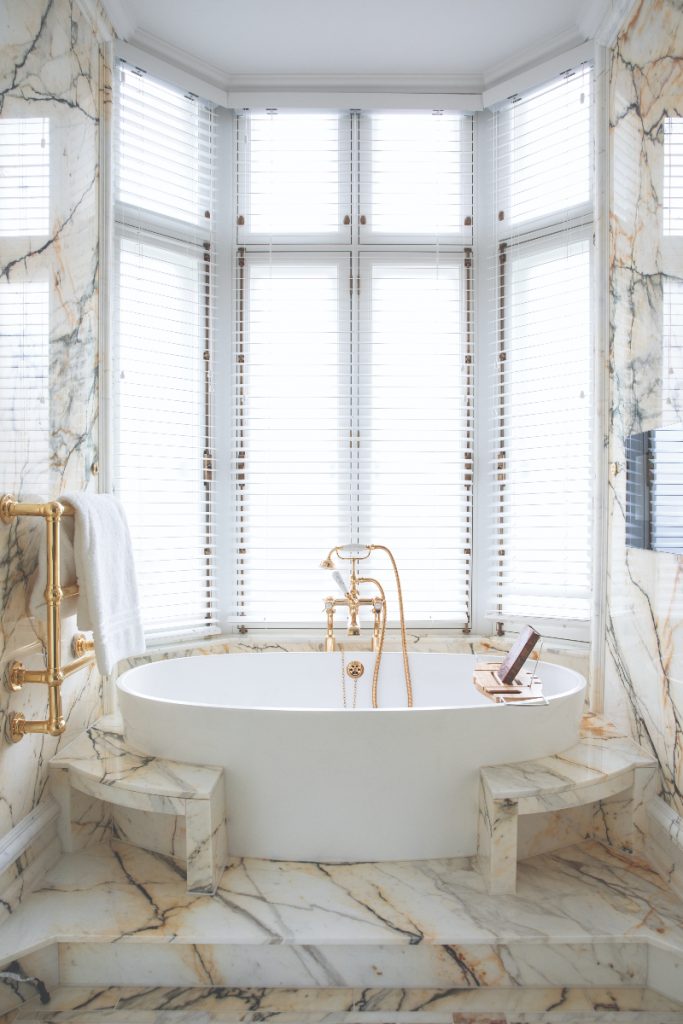 an Art Deco bathroom with gold marble and a large white freestanding bath
