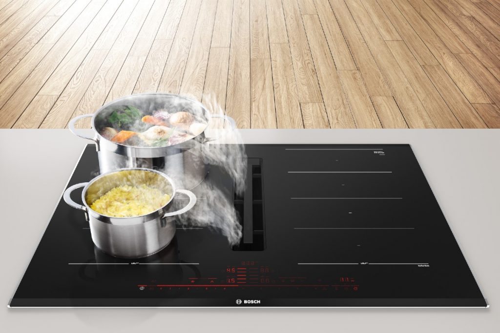 a hob with extractor in a kitchen with two stainless steel pans containing food steaming on top of it