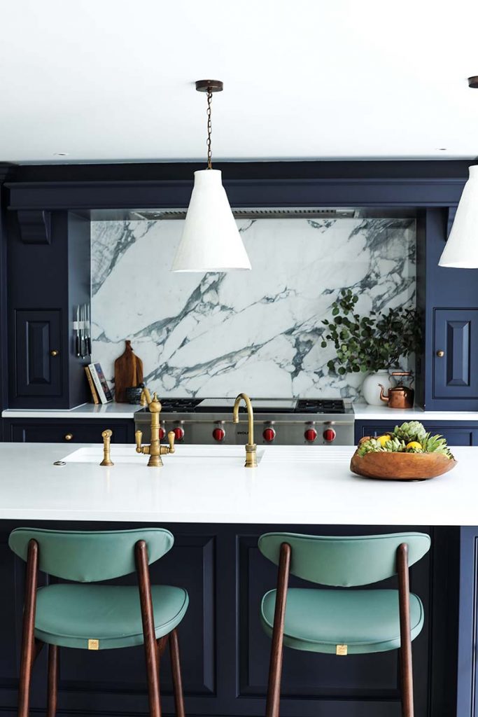 a kitchen featuring a marble cplashback, green chairs, navy cabinetry and brass taps