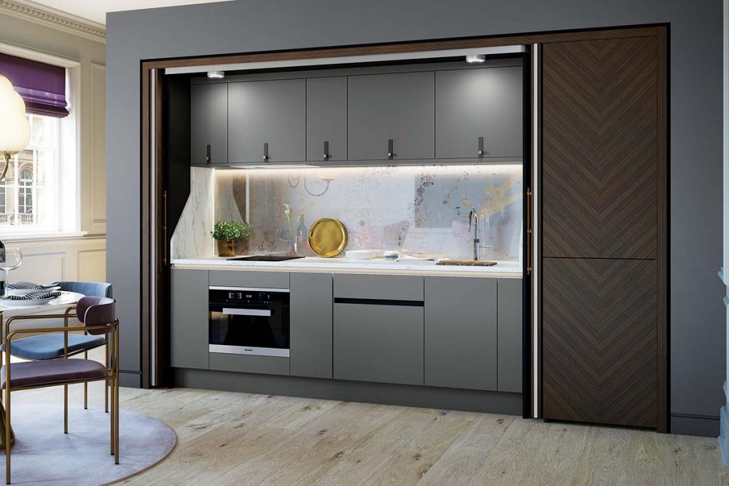 a hidden kitchen featuring walnut chevron-effect pocket bi-fold doors and grey cabinetry with black handles