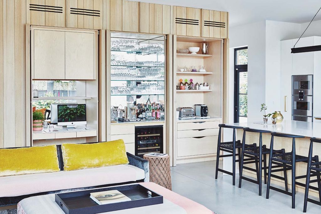 a hidden kitchen featuring ash cabinetry and black wooden bar stools at a white island