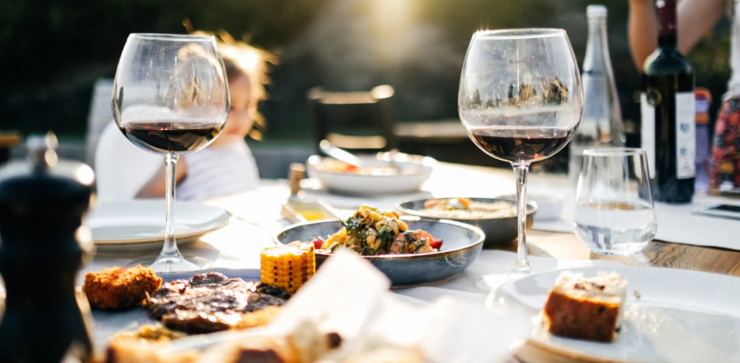a dining table featuring wine glasses and lots of food fresh from the barbecue