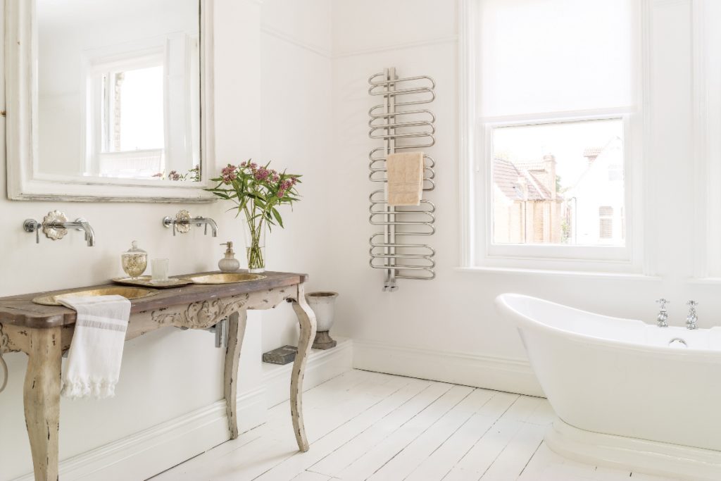 a traditional bathroom featuring a white roll top bath, an antique pedestal featuring two gold basins, and a large wall mirror