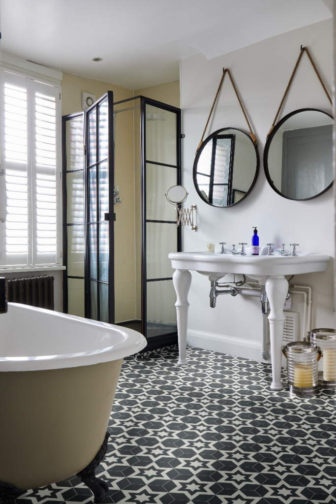 a traditional bathroom featuring monochrome floor tiles, a roll top bath, a pedestal basin and dark wood mirrors