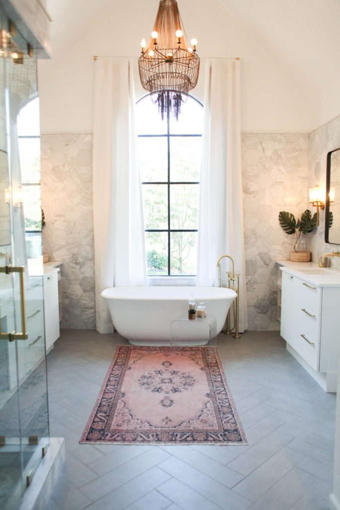 the Amiata bath under a black pendant light, with white cabinetry with brass handles, a pink and black rug and white linen curtains 