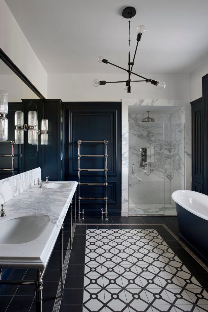 deep regal blue painted wall panelling, a marble shower and basins and monochrome floor tiles