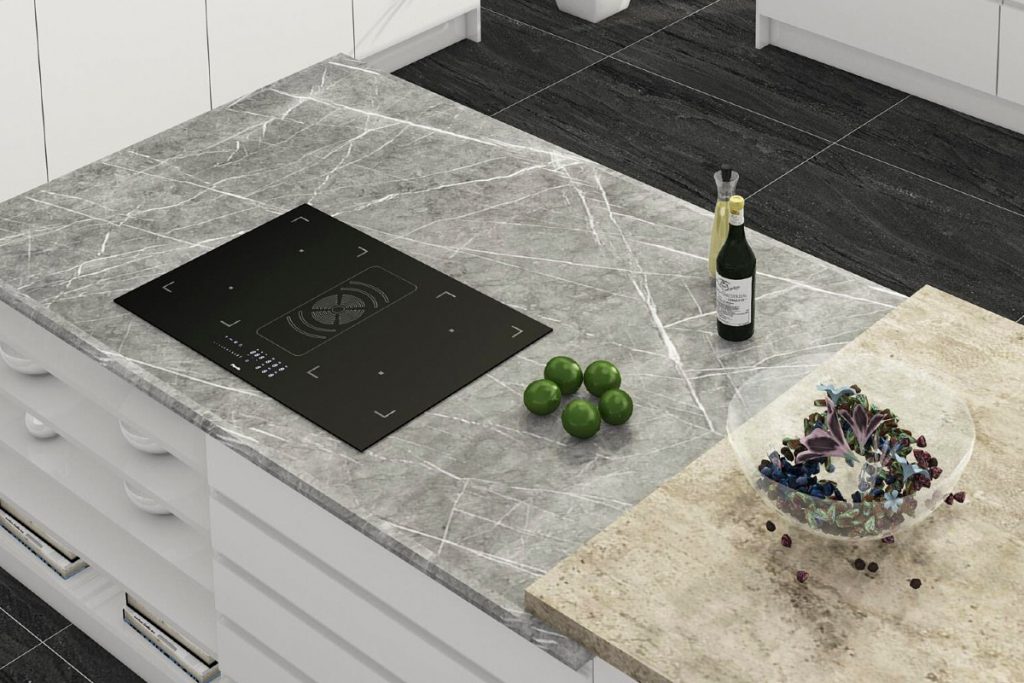 a hob with extractor in a kitchen set into a stone worktop with white cabinetry. There are five limes next to the cooker and bottles of olive oil and vinegar, as well as a bowl with salad