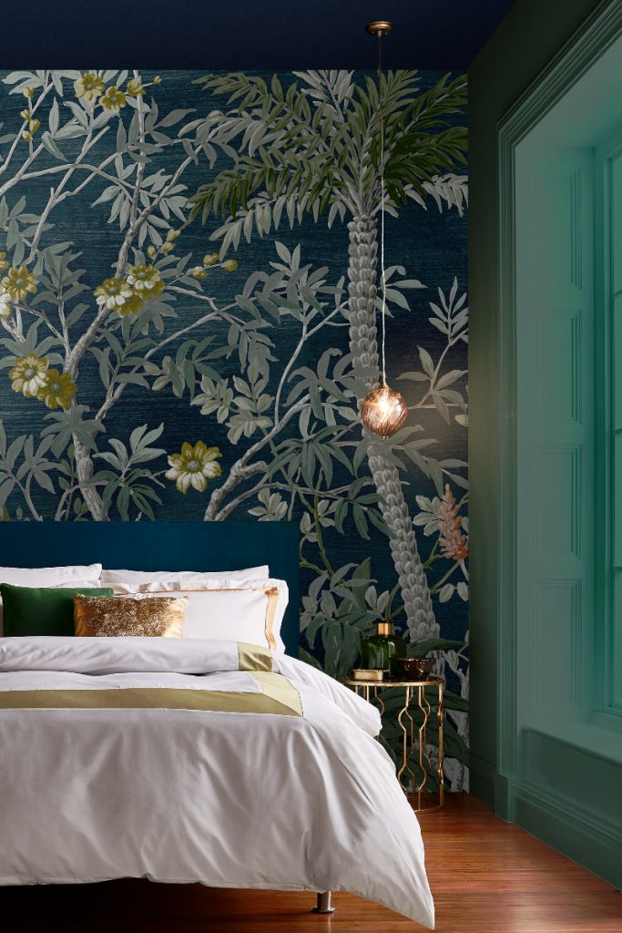 a green floral leaf mural behind a bed with gold accents
