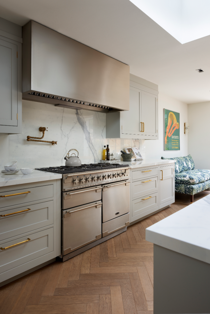 a kitchen layout with grey cabinetry with brass handles and a floral-print sofa