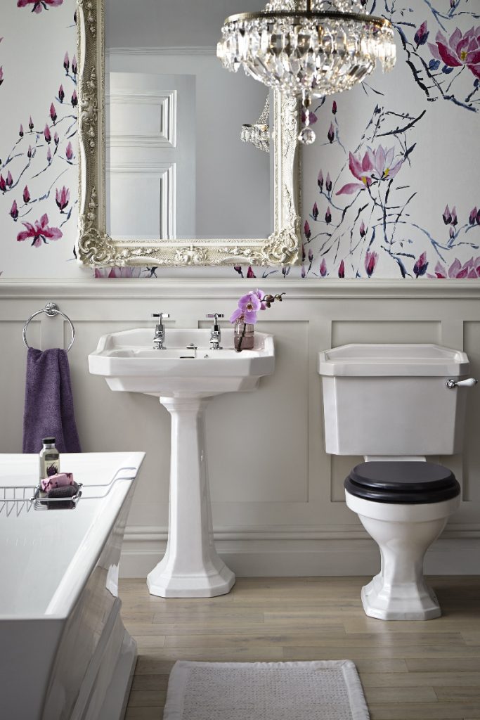 a traditional bathroom with floral wallpaper, a chandelier, a gilt mirror and a traditional pedestal basin and toilet