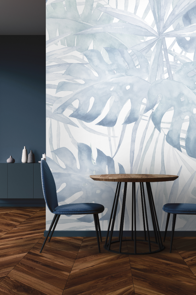 a pale tropical leaf mural in muted navy blue in front of a round wooden table and two navy chairs