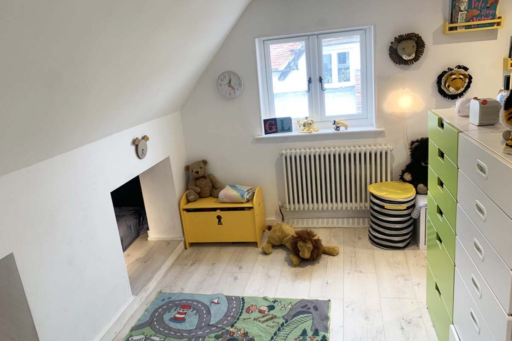 the finished kids' bedroom renovation with green and white storage, a traditional white radiator, a black and yellow laundry basket and a rug on the floor