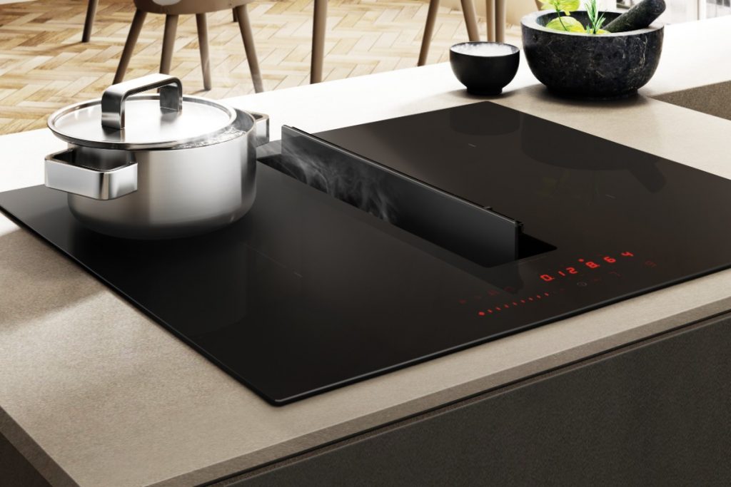 the Elica Nikolatesla FIT cooktop in a beige worktop featuring a stainless steel pan on top of it and some bowls with food in to the right