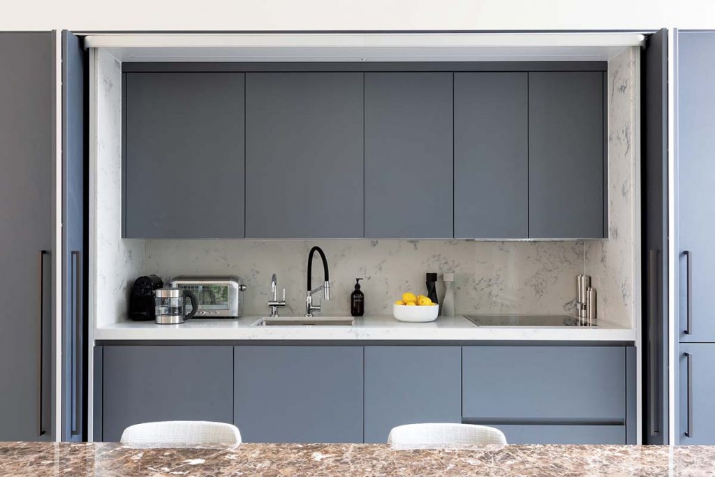 hidden kitchen cabinetry in a matt grey finish above a marble worktop