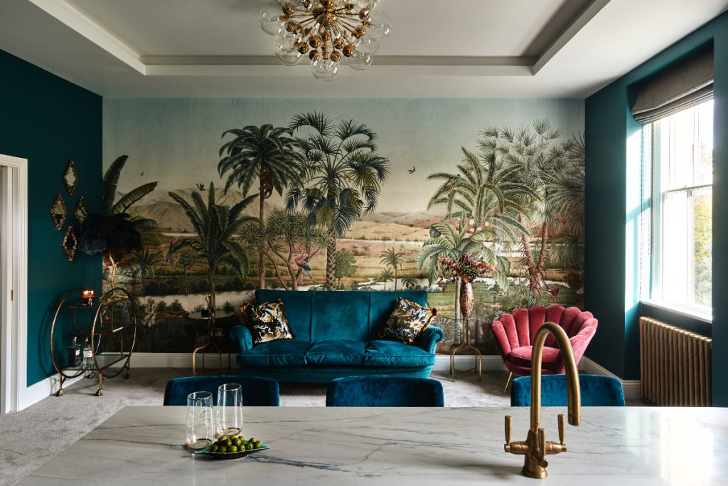 a tropical mural behind a teal sofa and pink shell armchair
