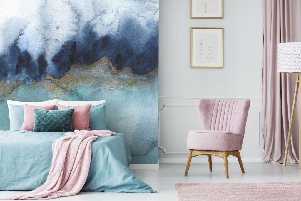 a navy, gold and powder blue mural design behind a bed in powder blue, teal and pink, with a pink chair next to them