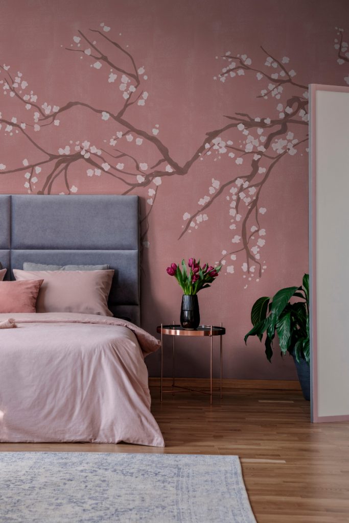 a pink blossom mural behind a modern bed and bedside table with a vase full of tulips on it