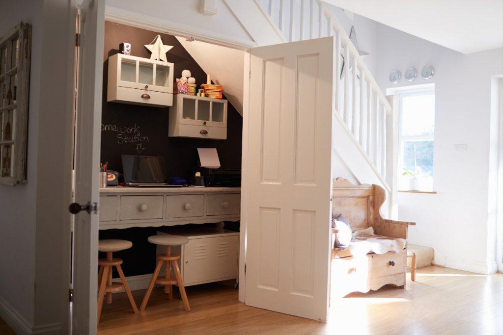 a space under a white flight of stairs used as an office and storage cupboard