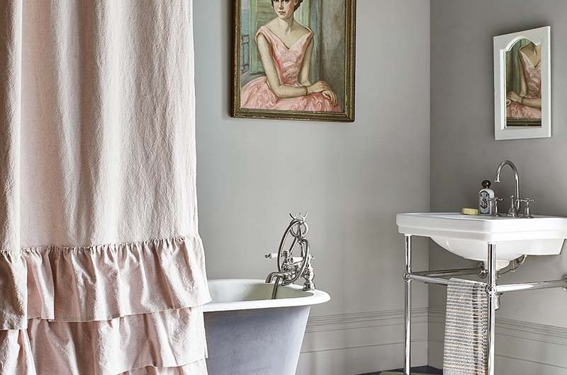A rustic bathroom featuring a traditional sink, a frilly pink shower curtain and antique paintings