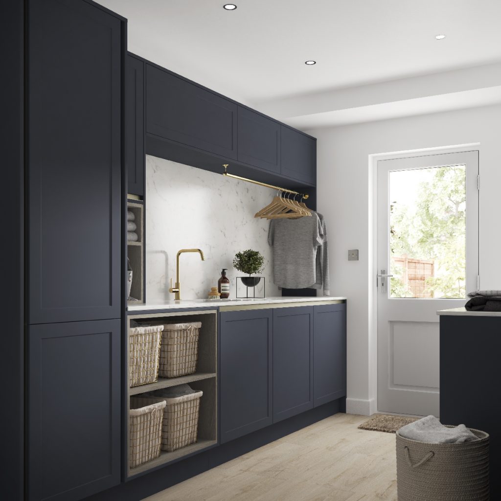 pull-out wash baskets in navy Shaker cabinetry, a brass tap in an undercounted sink, and a hanging rail with wooden hangers and clothes 