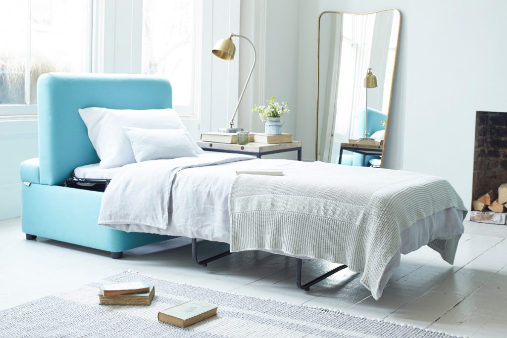 a guest bedroom with a blue sofa bed with bedding in neutral colours